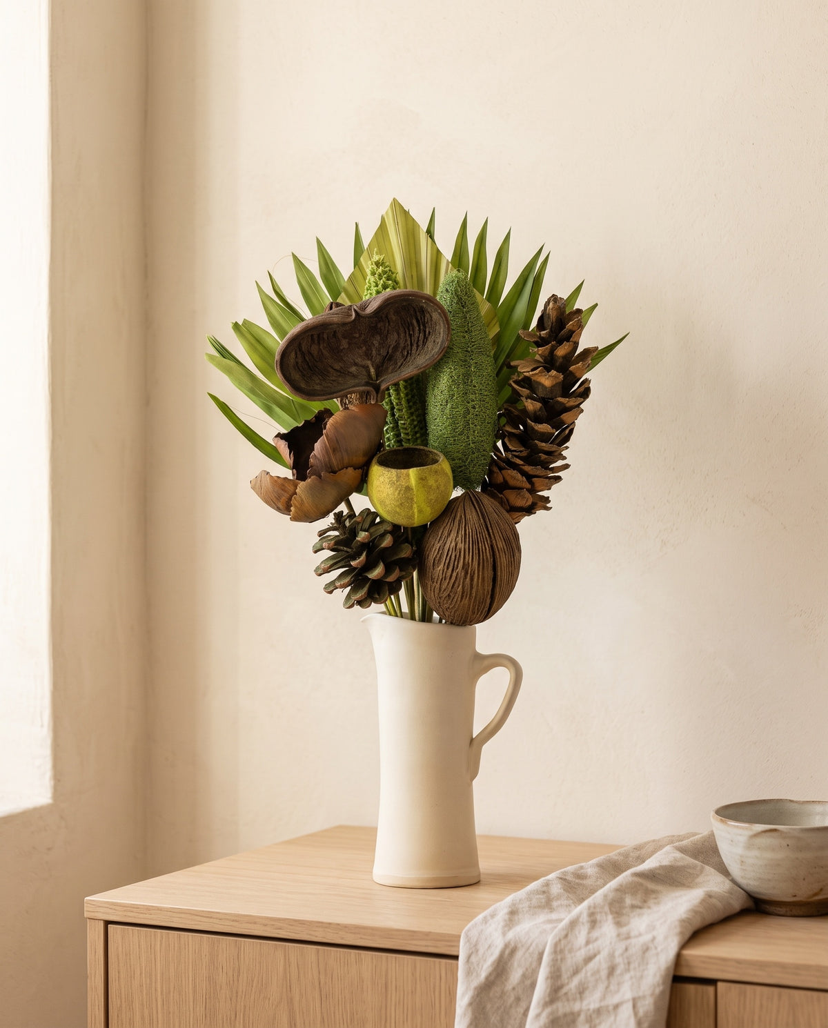 Ramo de flores secas em verde-pistácio com pinhas numa jarra sobre um aparador, ambiente de casa. Jarra não incluída.