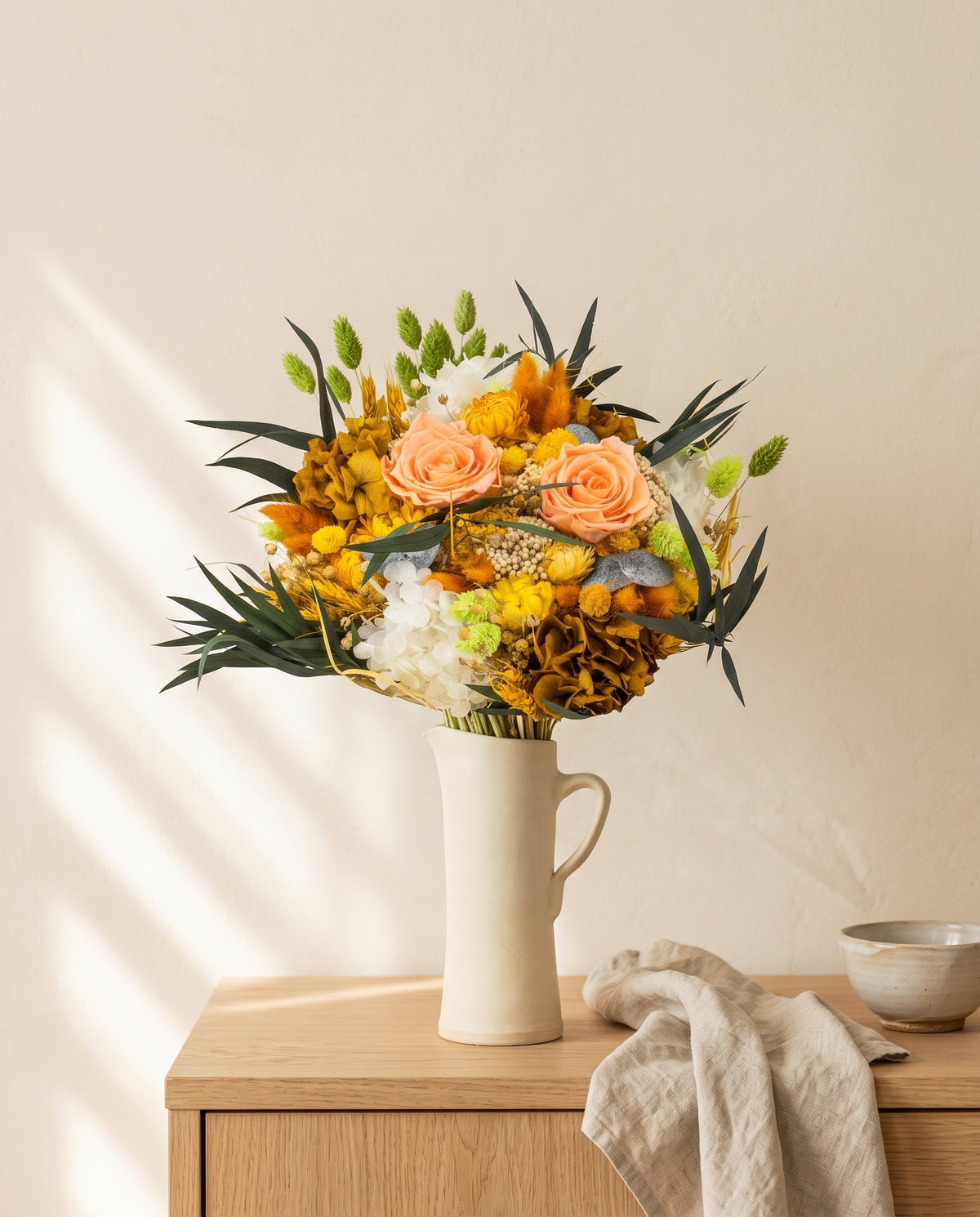 Ramo de flores secas y preservadas en amarillo en una jarra sobre un aparador, ambiente de casa. Jarra no incluida.