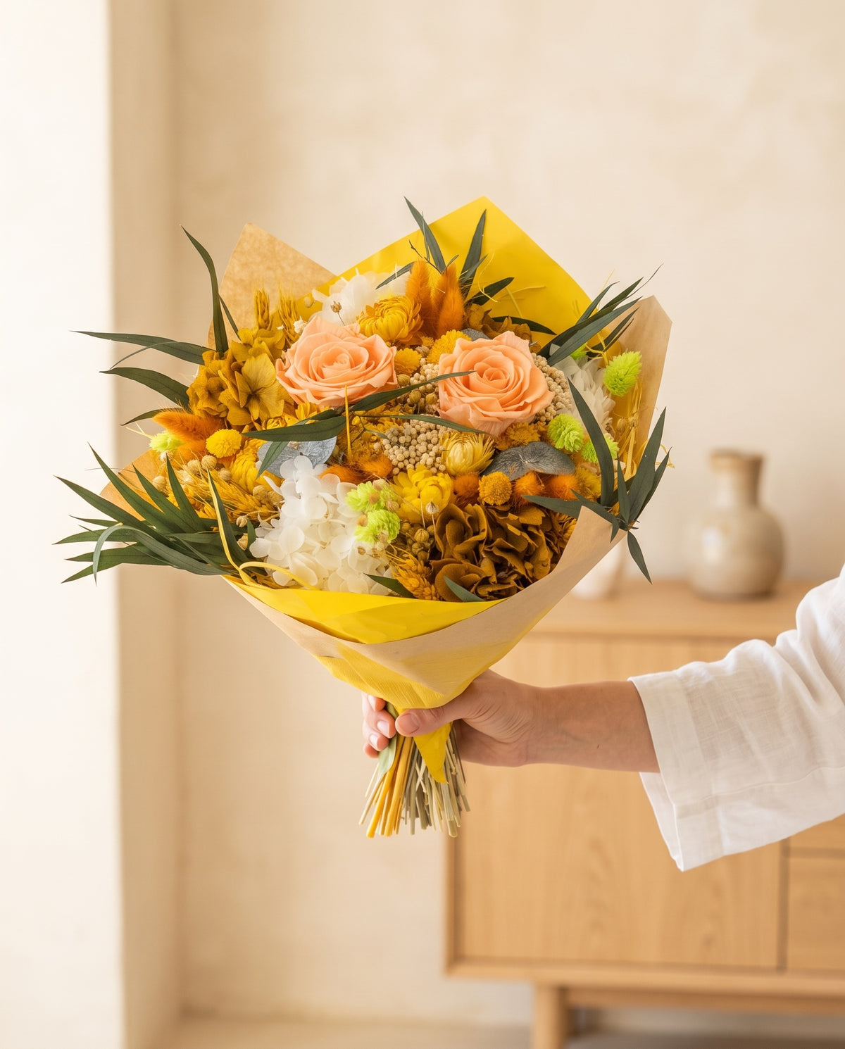 Mano sujetando el ramo de flores secas y preservadas en amarillo con su papel, como se entrega.