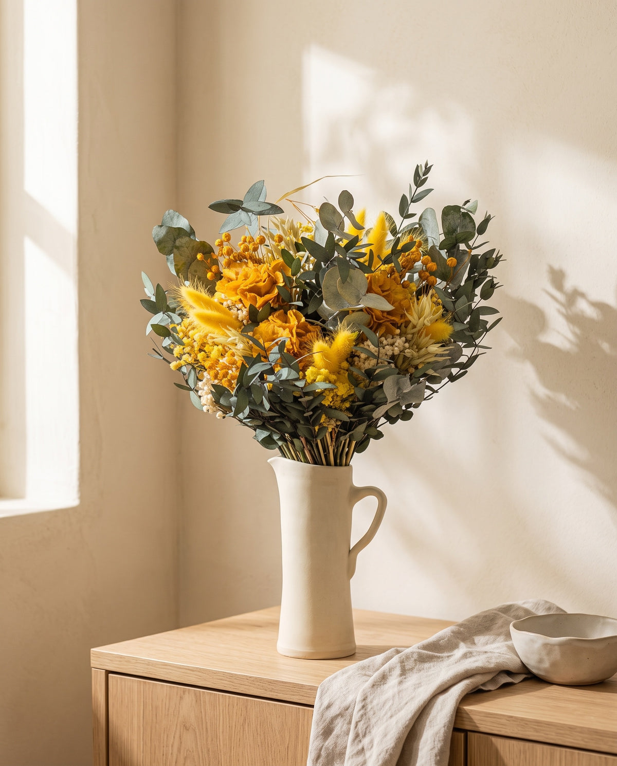 Ramo de flores secas y preservadas en amarillo en una jarra sobre un aparador, ambiente de casa. Jarra no incluida.