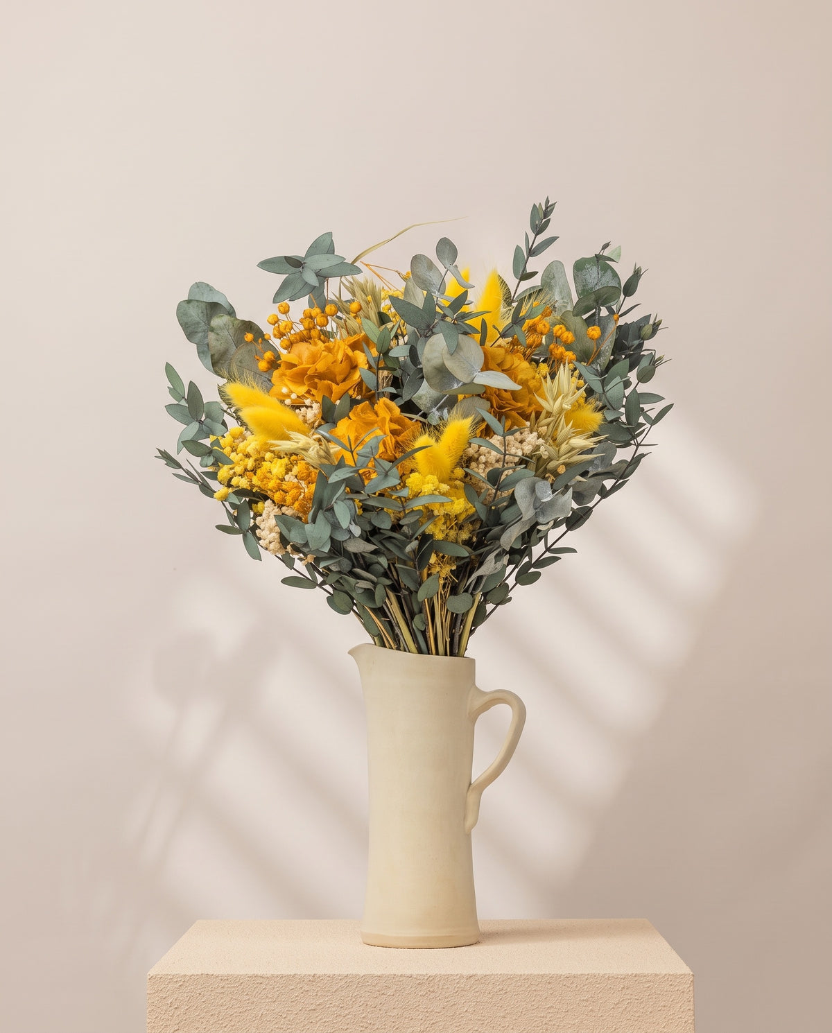 Ramo de flores secas y preservadas en amarillo en una jarra de cerámica crema. Jarra no incluida.