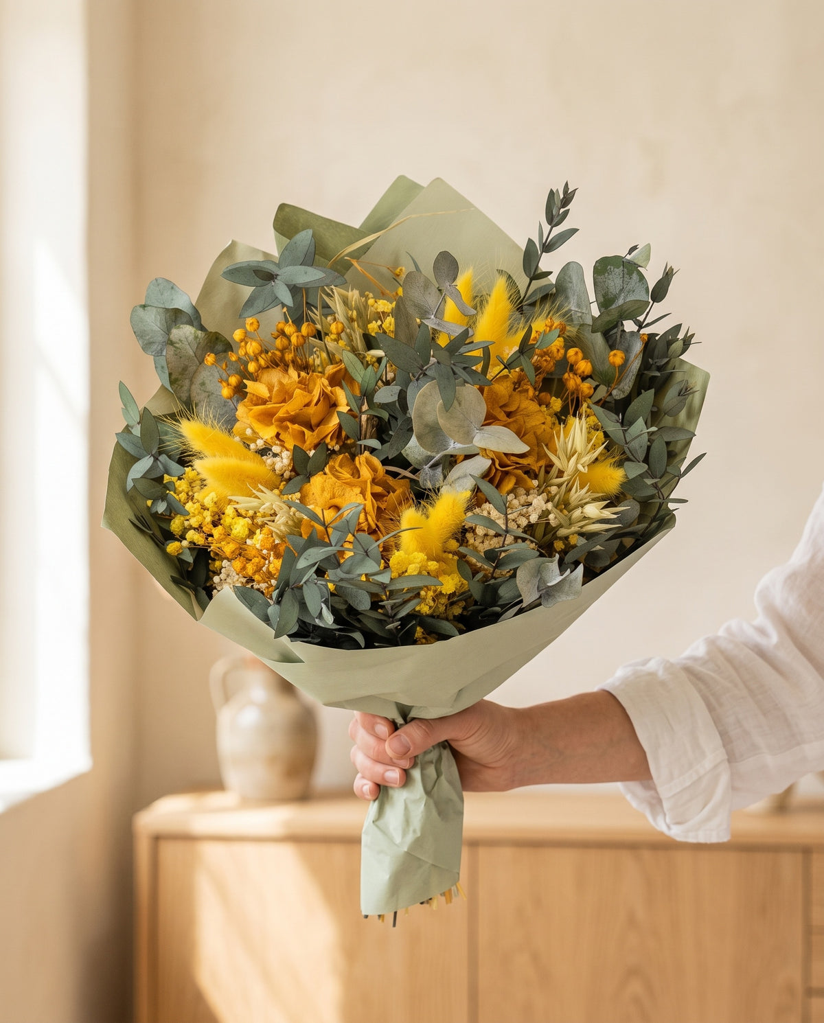 Mano sujetando el ramo de flores secas y preservadas en amarillo con su papel, como se entrega.