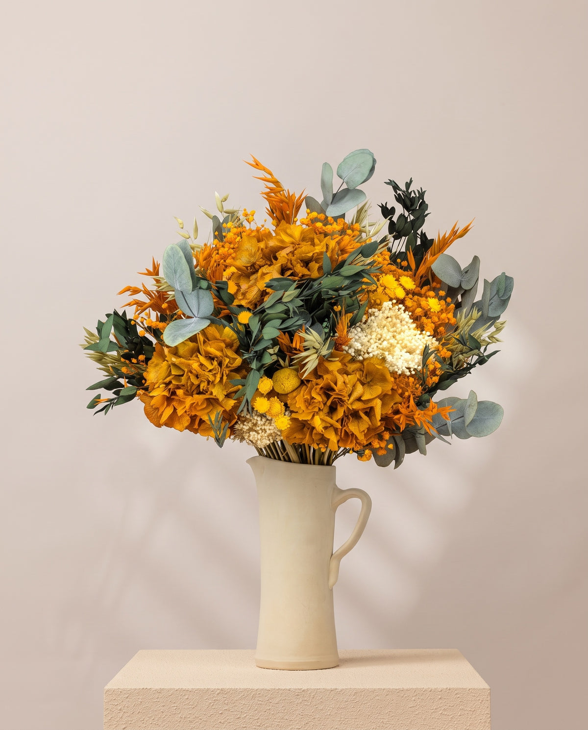 Ramo de flores secas y preservadas en amarillo y naranja en una jarra de cerámica crema. Jarra no incluida.
