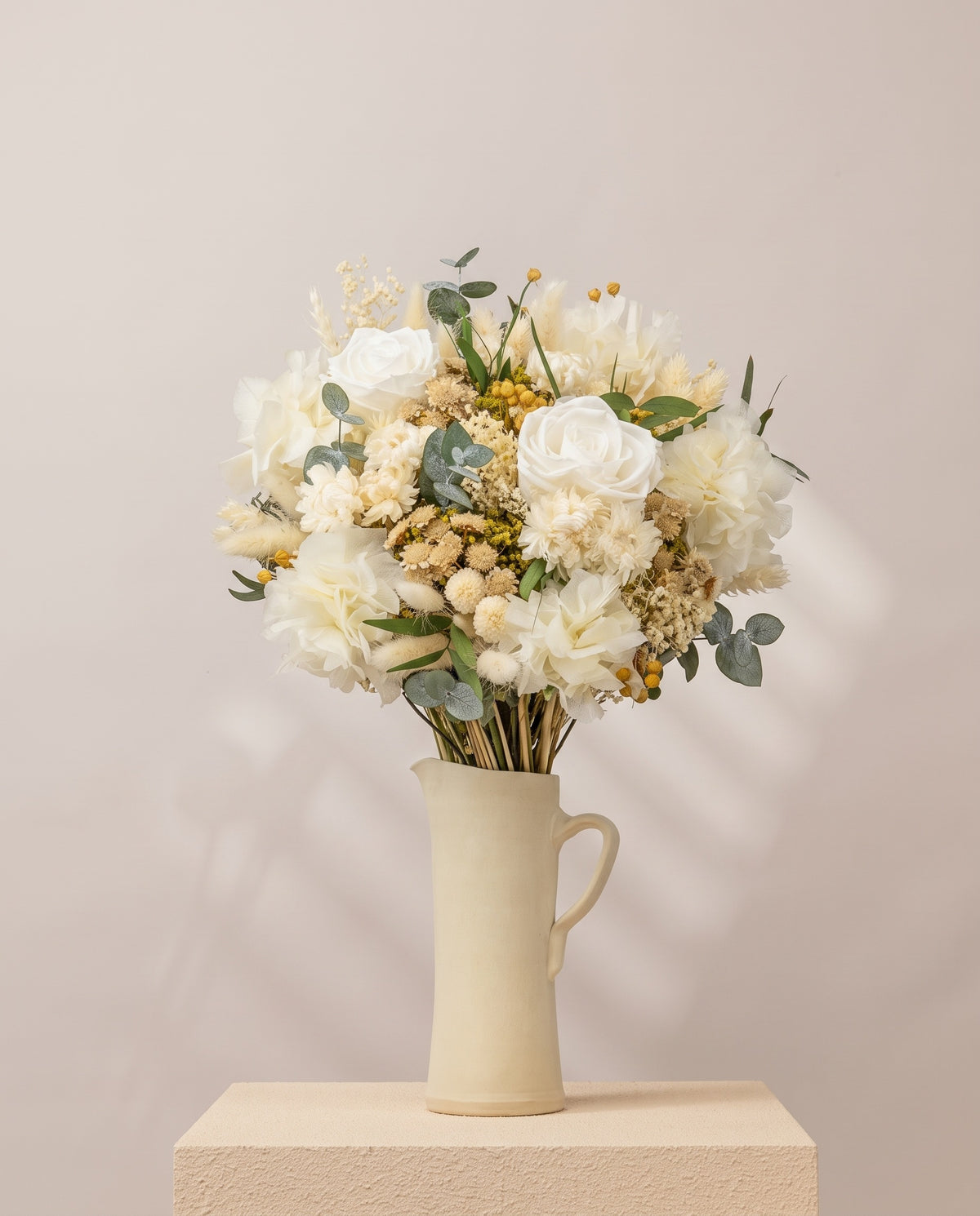 Ramo de flores secas y preservadas en blanco con rosas en una jarra de cerámica crema. Jarra no incluida.
