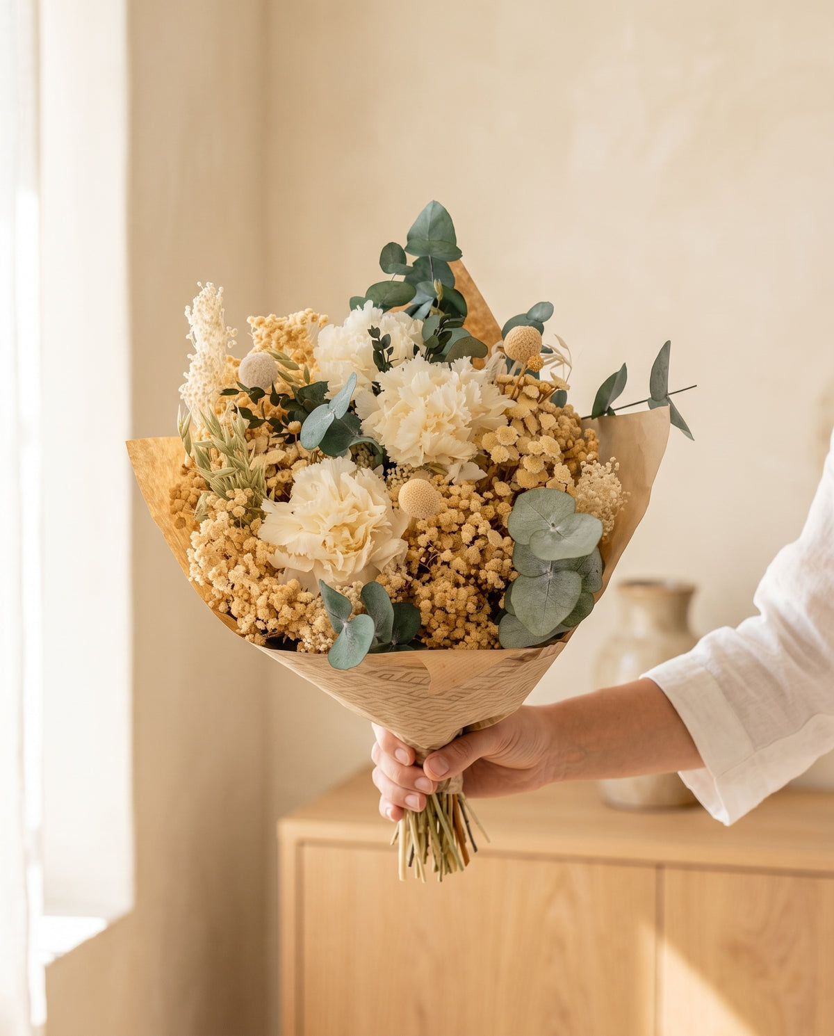 Mano sujetando el ramo de flores secas y preservadas en blanco con su papel, como se entrega.