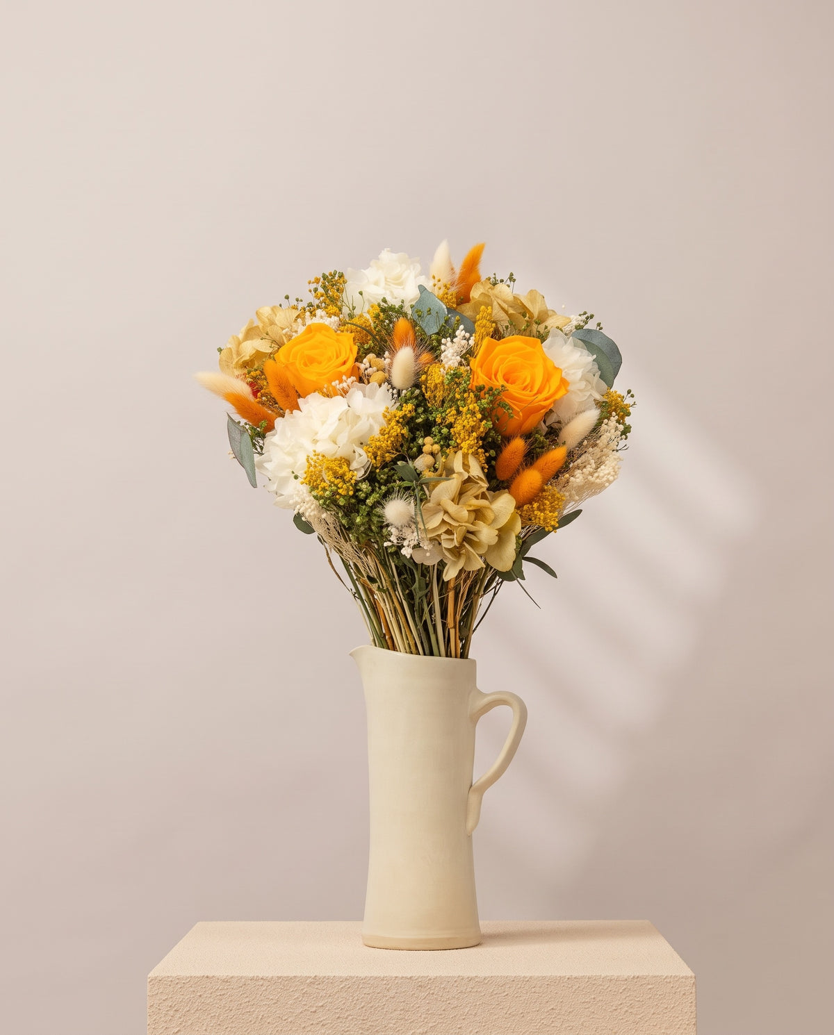 Ramo de flores secas y preservadas en blanco y naranja en una jarra de cerámica crema. Jarra no incluida.