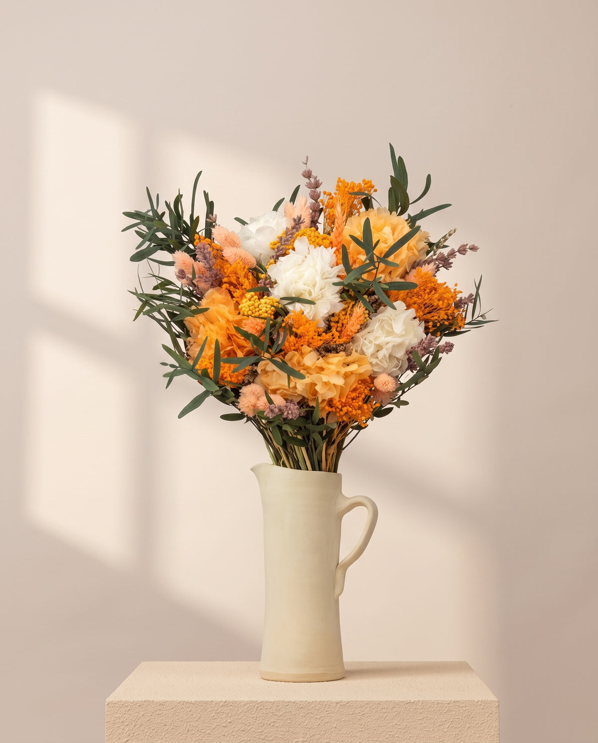 Ramo de flores secas y preservadas en blanco y naranja en una jarra de cerámica crema. Jarra no incluida.