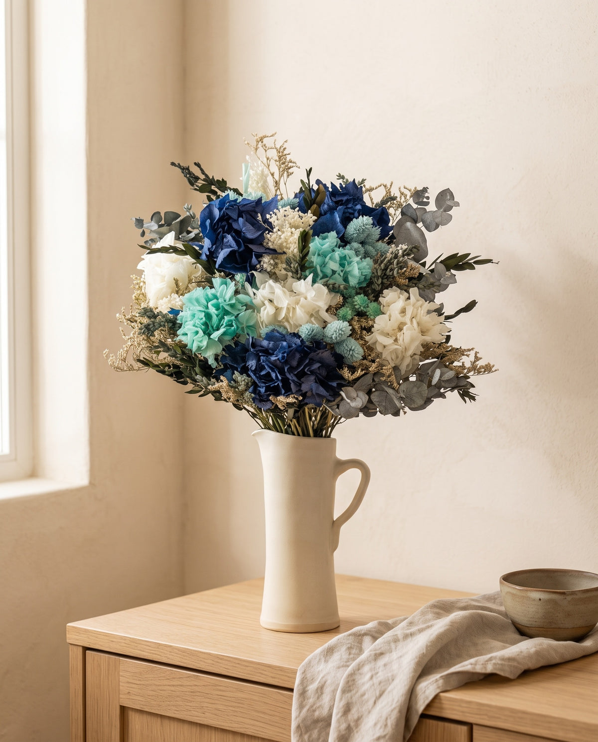 Ramo de flores secas y preservadas en celeste con hortensia en una jarra sobre un aparador, ambiente de casa. Jarra no incluida.