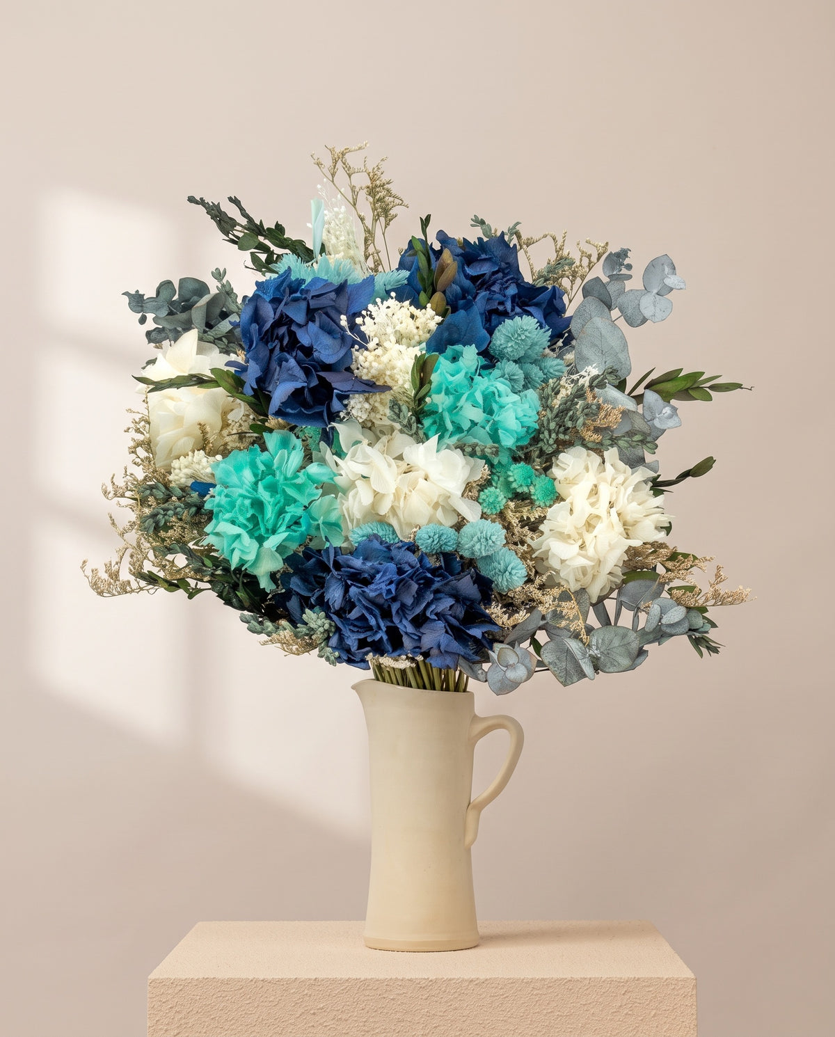 Ramo de flores secas y preservadas en celeste con hortensia en una jarra de cerámica crema. Jarra no incluida.