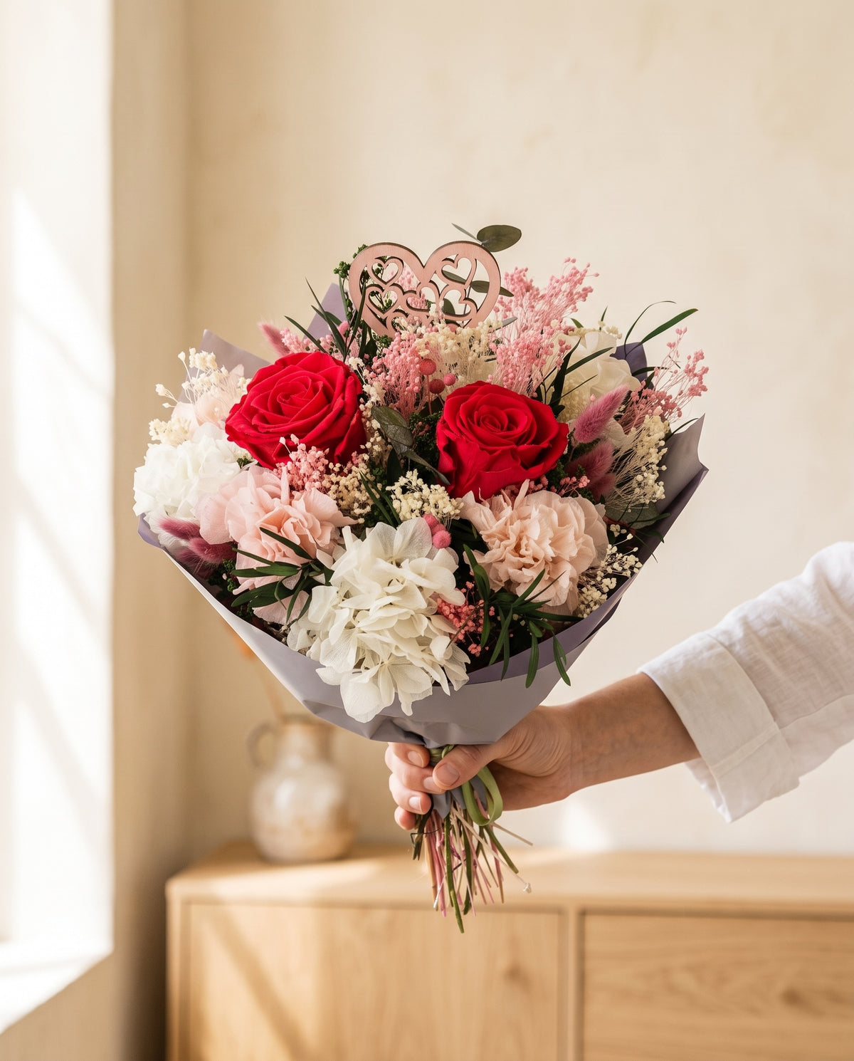 Mano sujetando el ramo de flores secas y preservadas en cereza con su papel, como se entrega.