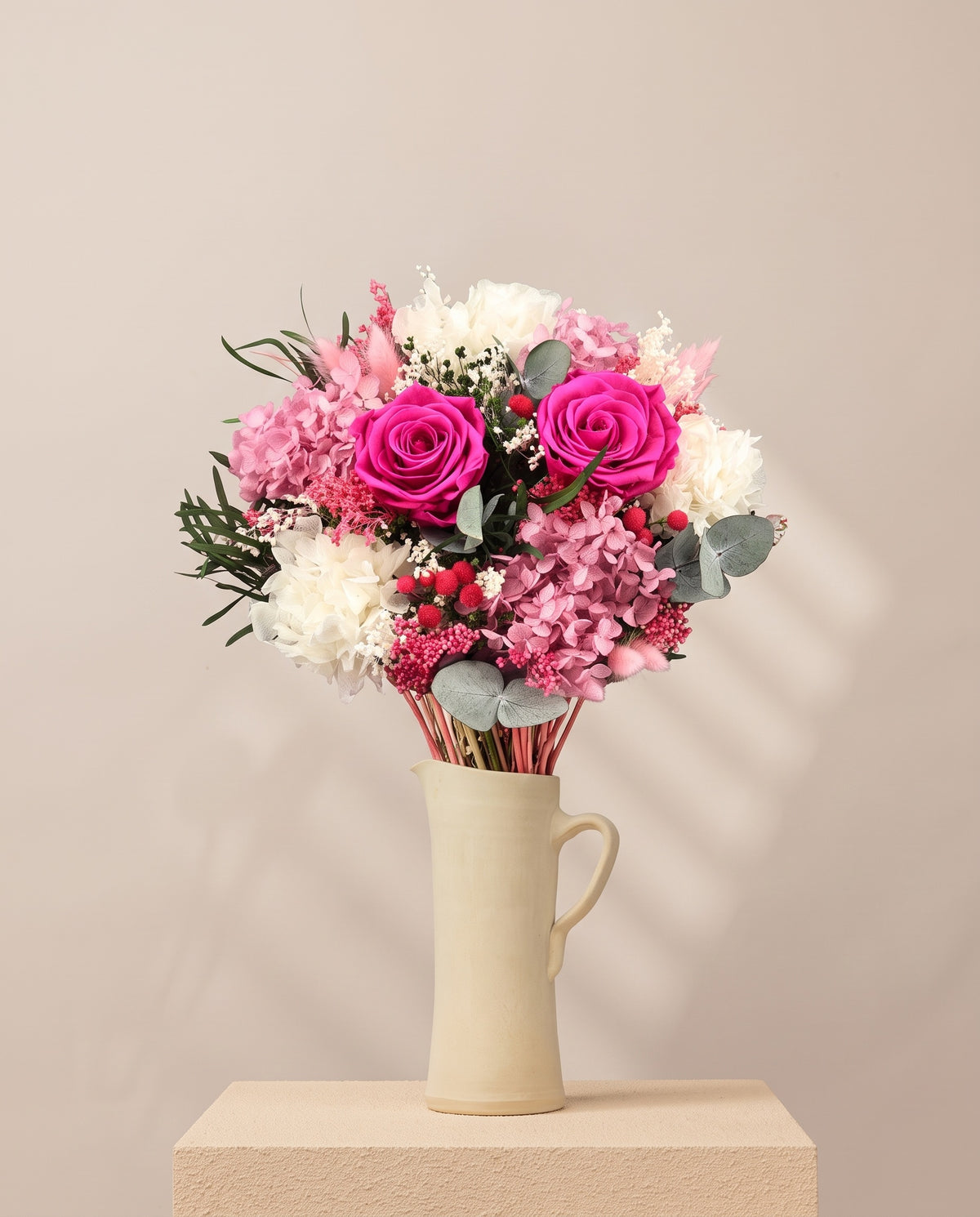 Ramo de flores secas y preservadas en fucsia y rosa en una jarra de cerámica crema. Jarra no incluida.