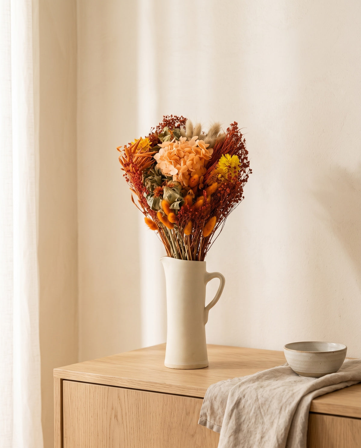 Ramo de flores secas y preservadas en naranja con hortensia en una jarra sobre un aparador, ambiente de casa. Jarra no incluida.