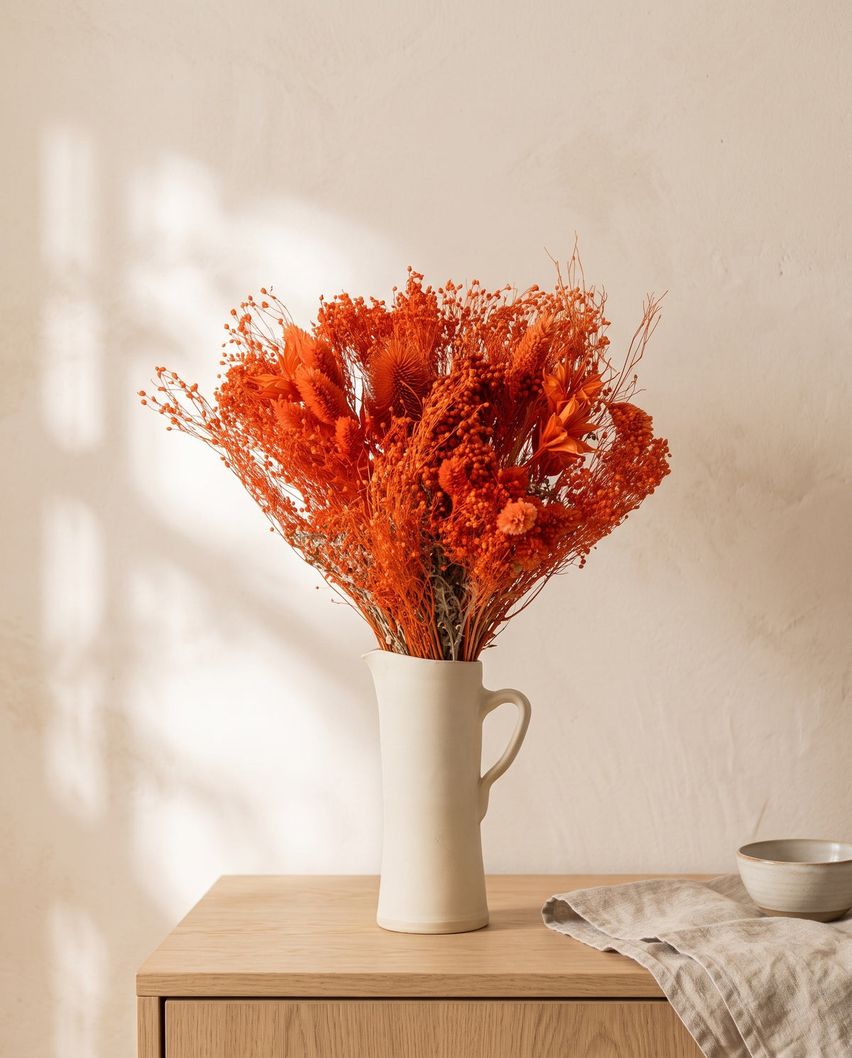 Ramo de flores secas y preservadas en naranja con paniculata en una jarra sobre un aparador, ambiente de casa. Jarra no incluida.