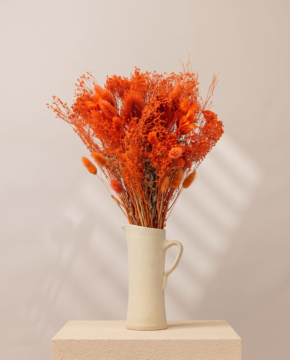 Ramo de flores secas y preservadas en naranja con paniculata en una jarra de cerámica crema. Jarra no incluida.