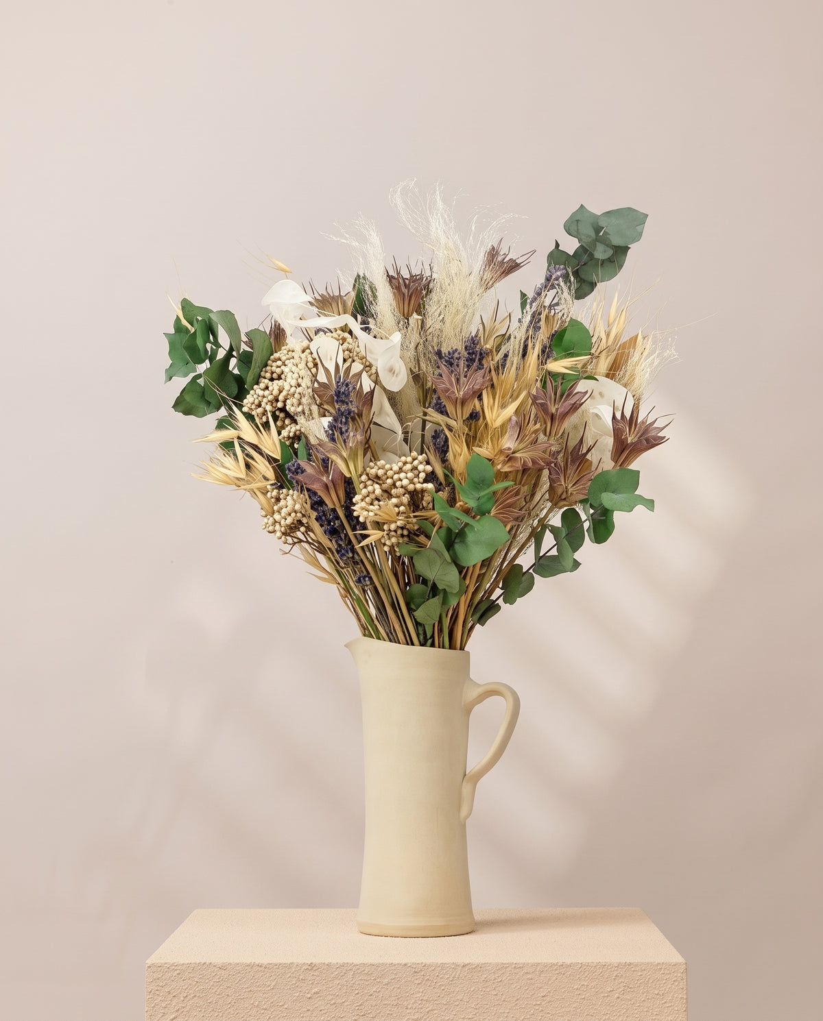 Ramo de flores secas e preservadas em tons naturais numa jarra de cerâmica creme. Jarra não incluída.