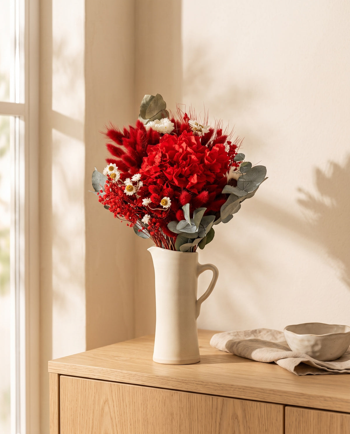 Ramo de flores secas y preservadas en rojo con hortensia en una jarra sobre un aparador, ambiente de casa. Jarra no incluida.