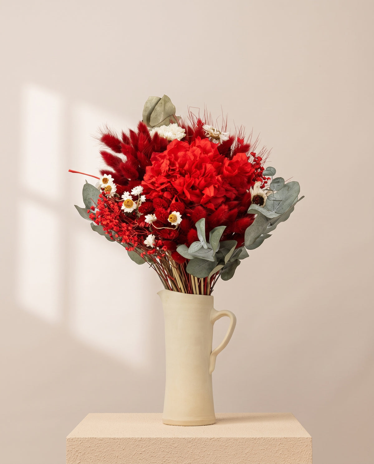 Ramo de flores secas y preservadas en rojo con hortensia en una jarra de cerámica crema. Jarra no incluida.