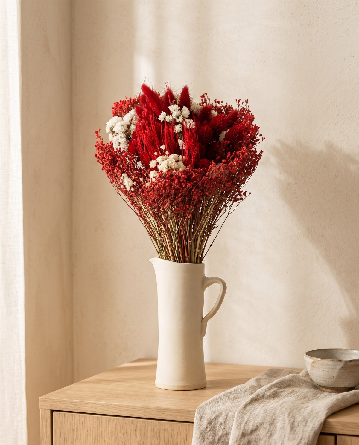 Ramo de flores secas y preservadas en rojo con lagurus en una jarra sobre un aparador, ambiente de casa. Jarra no incluida.
