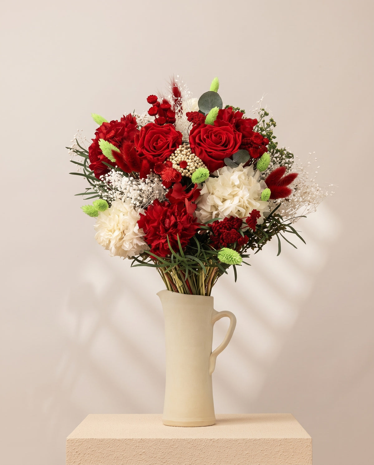 Ramo de flores secas y preservadas en rojo con rosas en una jarra de cerámica crema. Jarra no incluida.
