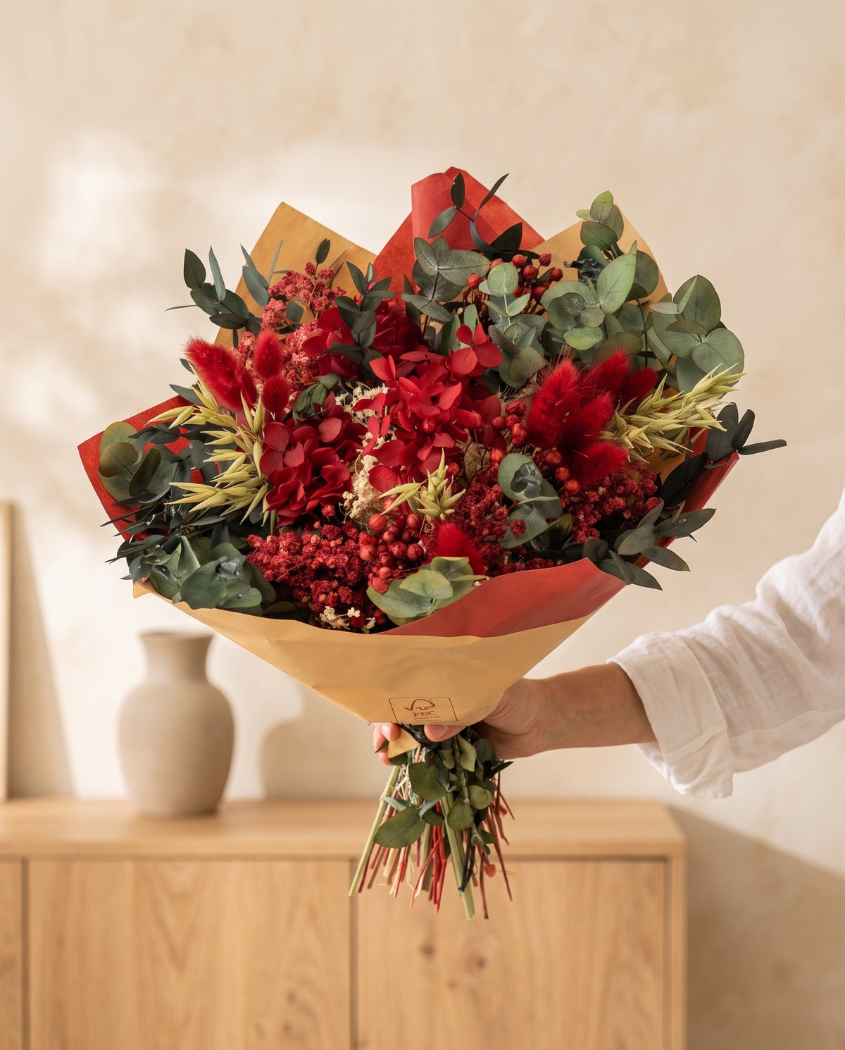 Mano sujetando el ramo de flores secas y preservadas en rojo con su papel, como se entrega.