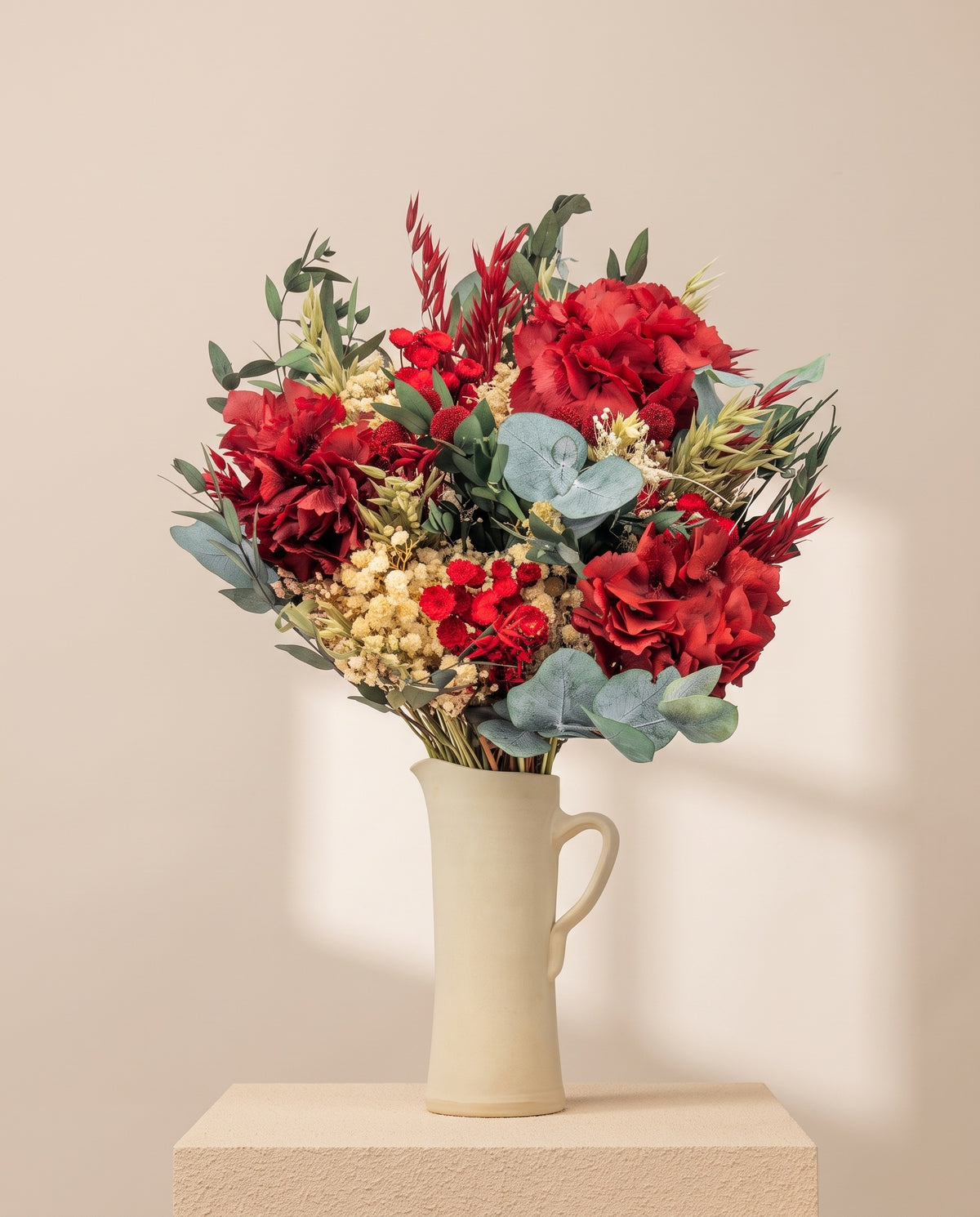 Ramo de flores secas y preservadas en rojo en una jarra de cerámica crema. Jarra no incluida.