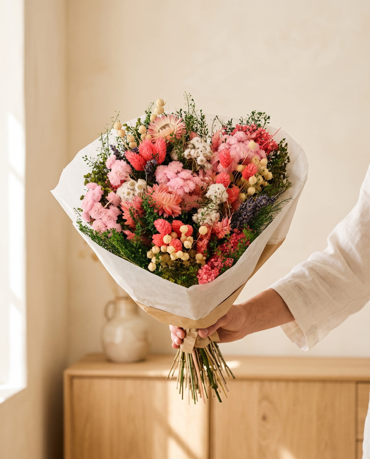 Mano sujetando el ramo de flores secas y preservadas en rosa con su papel, como se entrega.