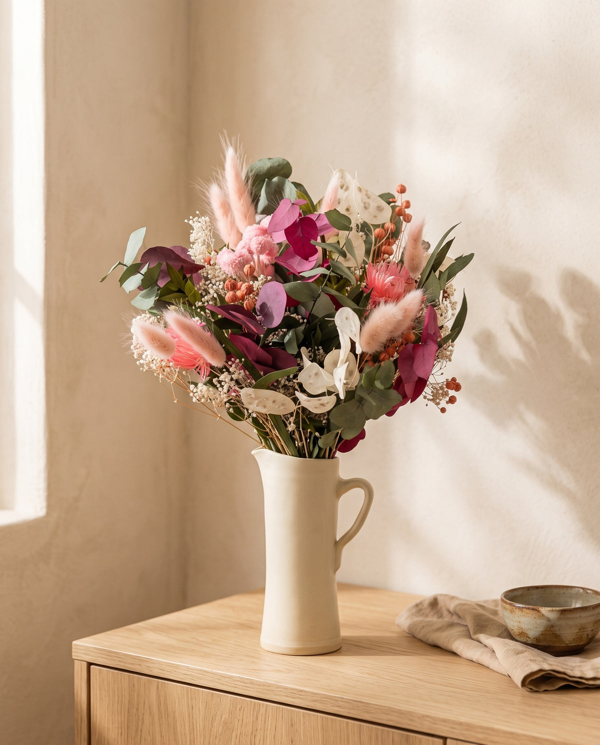 Ramo de flores secas y preservadas en rosa con eucalipto en una jarra sobre un aparador, ambiente de casa. Jarra no incluida.