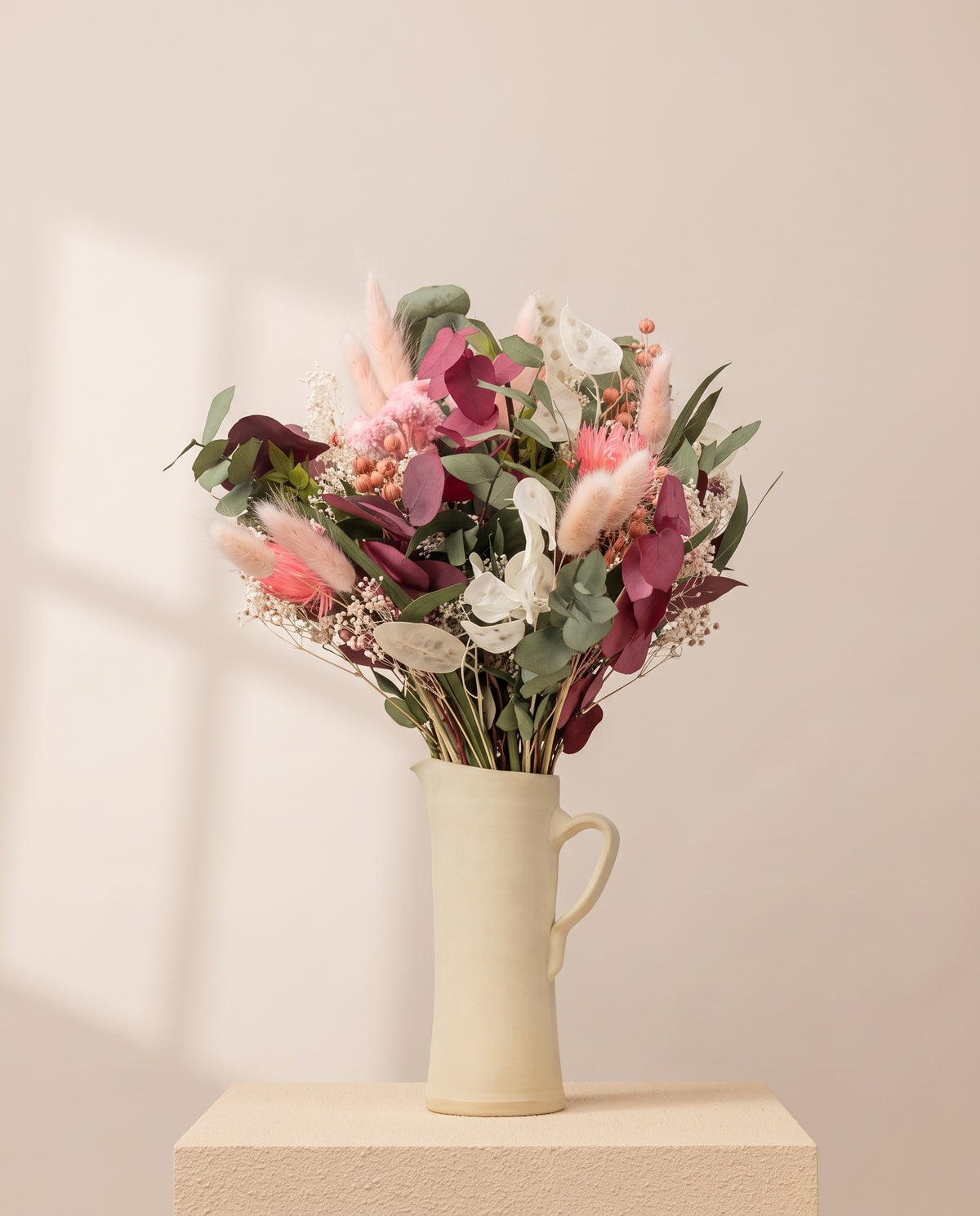 Ramo de flores secas y preservadas en rosa con eucalipto en una jarra de cerámica crema. Jarra no incluida.
