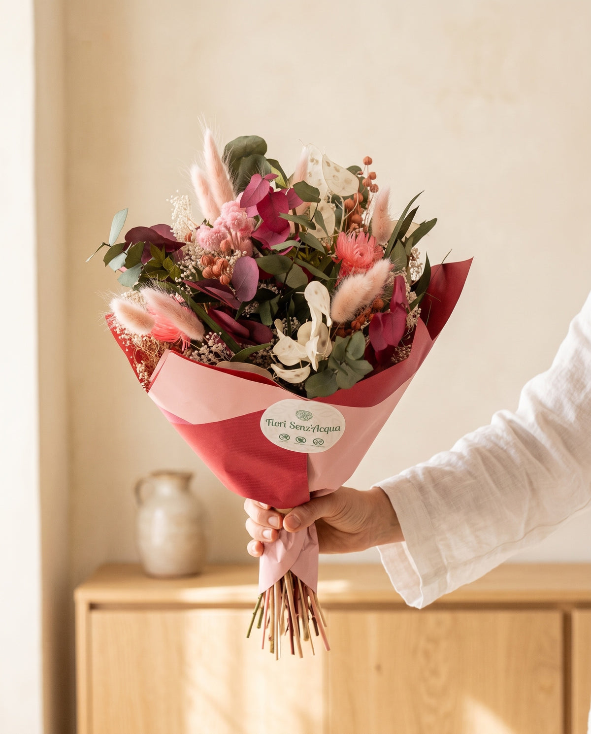 Mano sujetando el ramo de flores secas y preservadas en rosa con eucalipto con su papel, como se entrega.