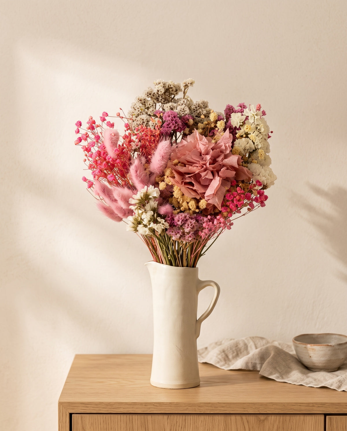 Ramo de flores secas y preservadas en rosa con hortensia en una jarra sobre un aparador, ambiente de casa. Jarra no incluida.