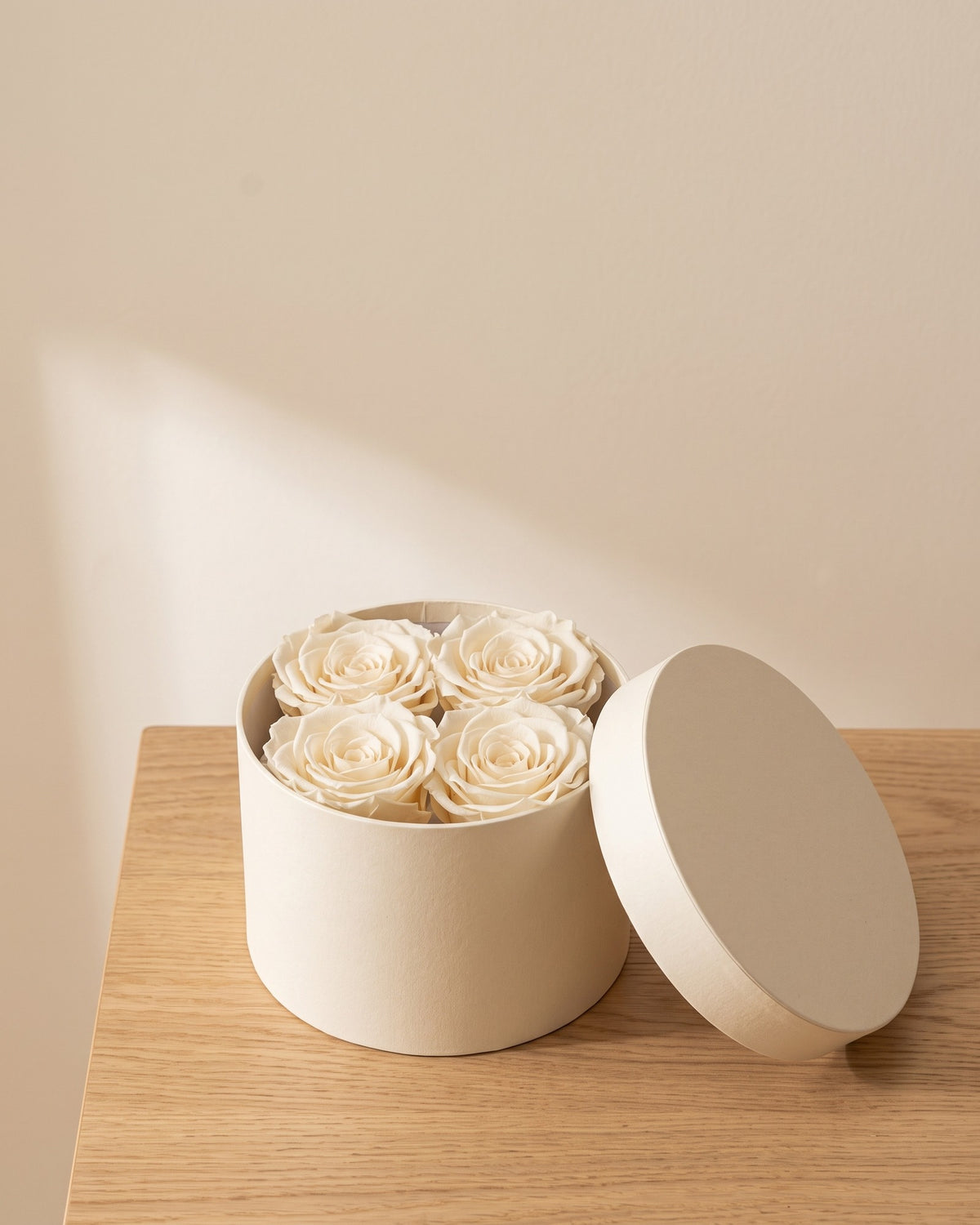 Cabeças de rosa preservada branca numa caixa redonda de oferta, em ambiente decorado. Caixa de oferta não incluída.