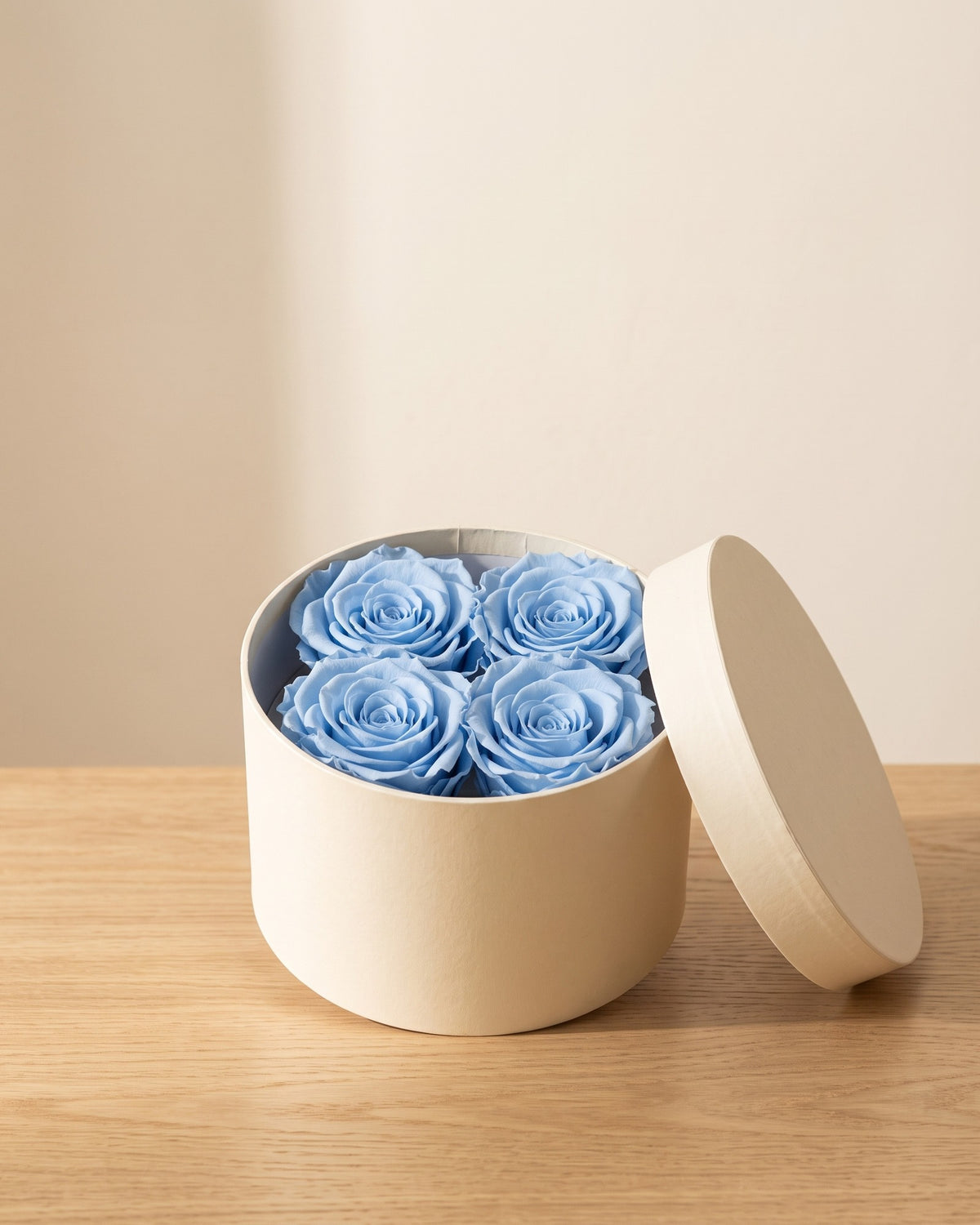 Cabeças de rosa preservada azul-celeste numa caixa redonda de oferta, em ambiente decorado. Caixa de oferta não incluída.