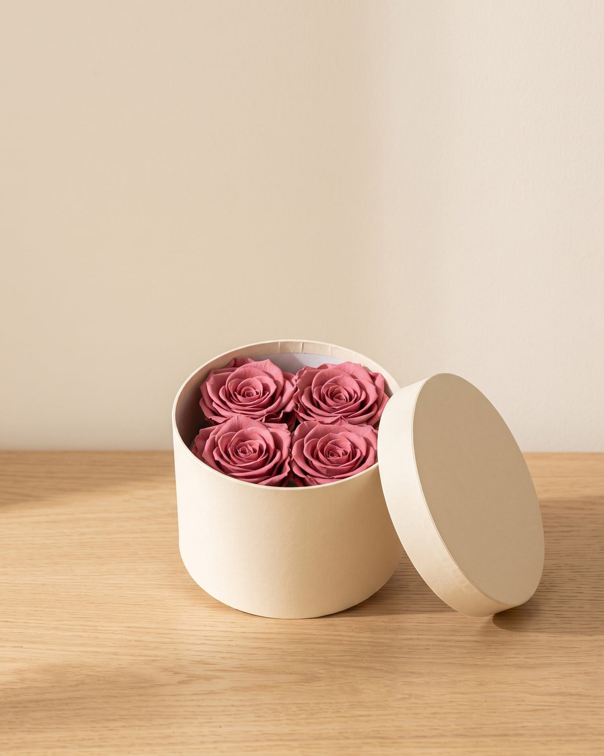 Cabeças de rosa preservada cereja numa caixa redonda de oferta, em ambiente decorado. Caixa de oferta não incluída.