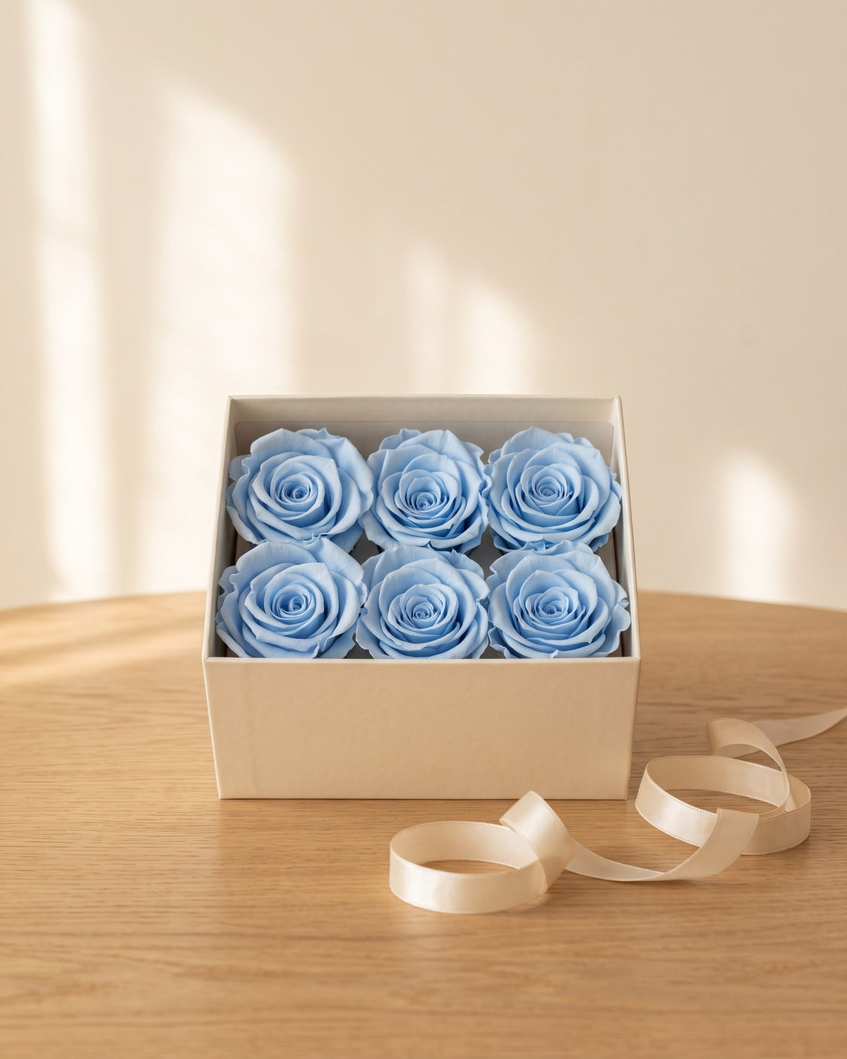 Cabezas de rosa preservada celeste en una caja de regalo, ambientada. Caja de regalo no incluida.