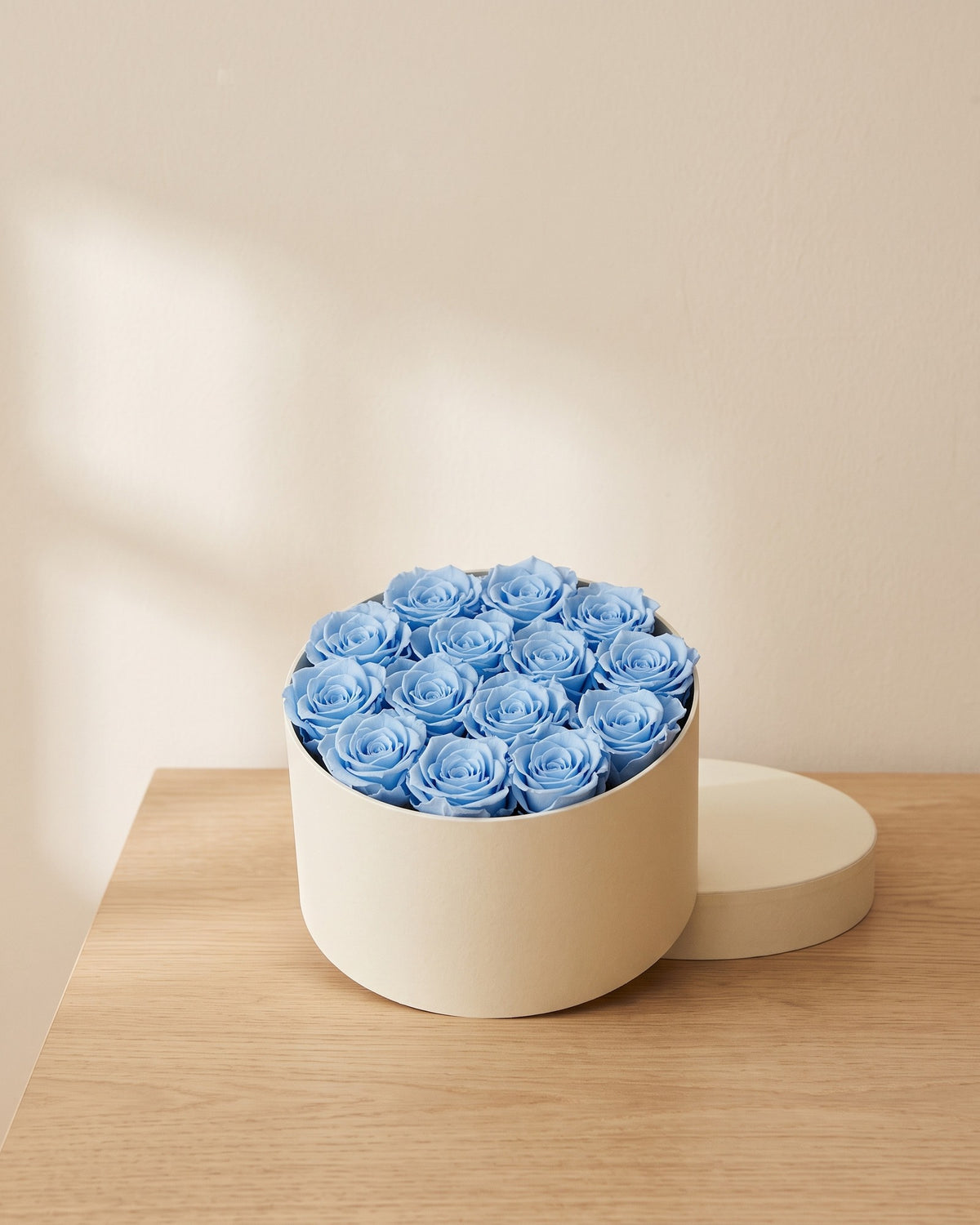 Cabezas de rosa preservada azul clara en una caja redonda de regalo, ambientada. Caja de regalo no incluida.