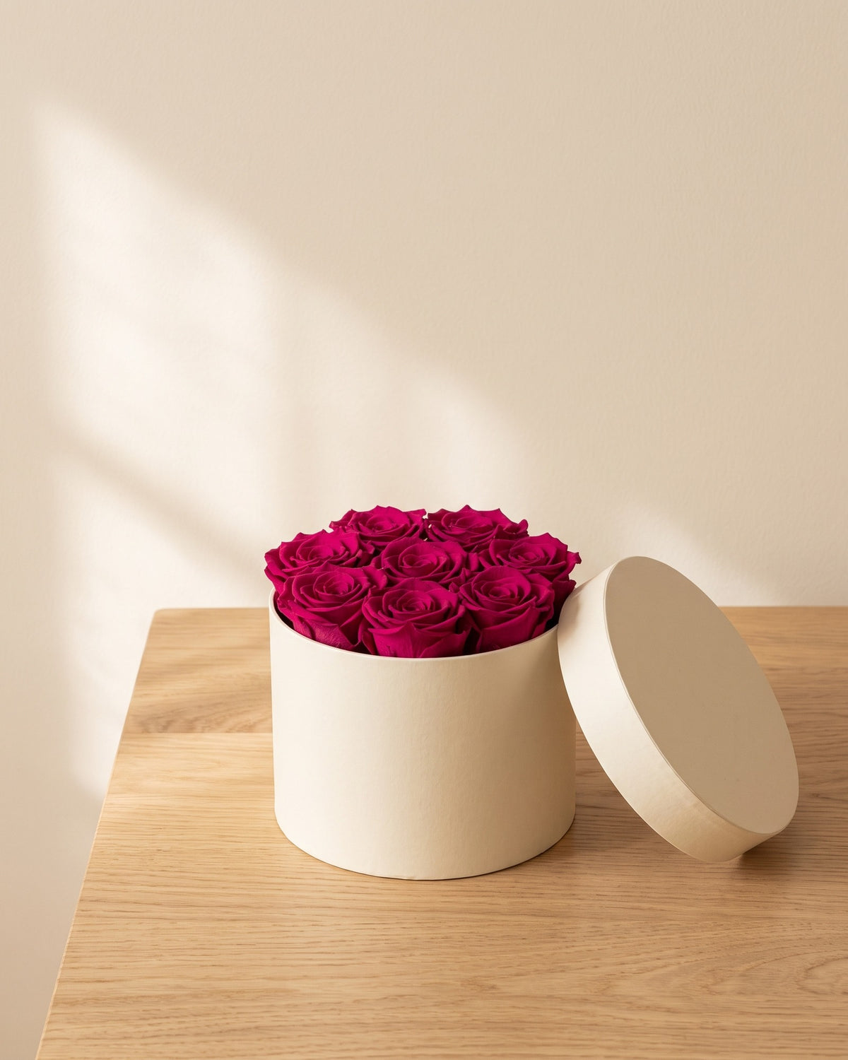 Cabezas de rosa preservada fucsia en una caja redonda de regalo, ambientada. Caja de regalo no incluida.