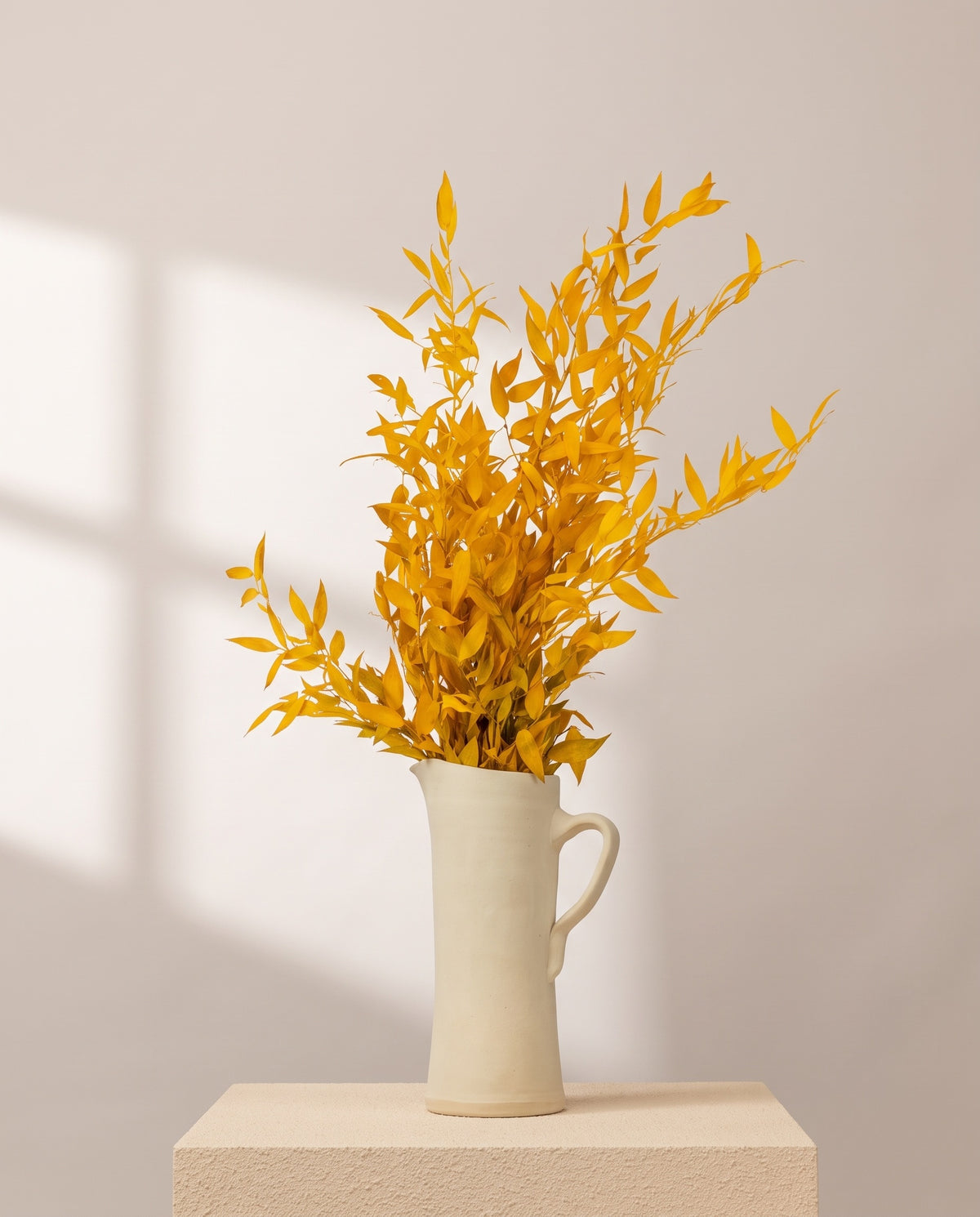 Ruscus preservado amarillo en una jarra de cerámica crema, ambientado. Jarra no incluida.