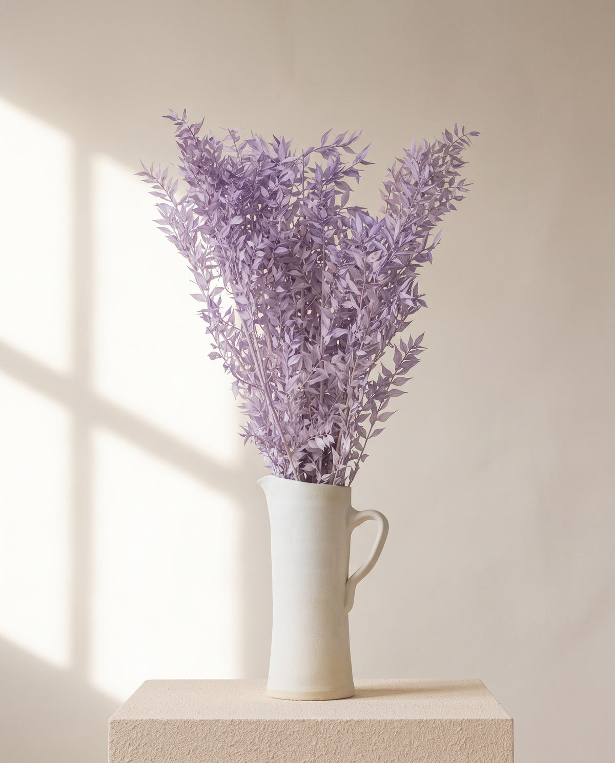 Ruscus preservado lavanda en una jarra de cerámica crema, ambientado. Jarra no incluida.