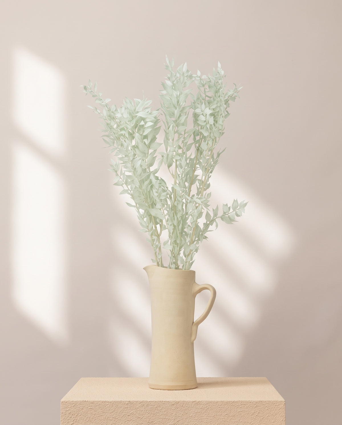 Ruscus preservado verde mint en una jarra de cerámica crema, ambientado. Jarra no incluida.
