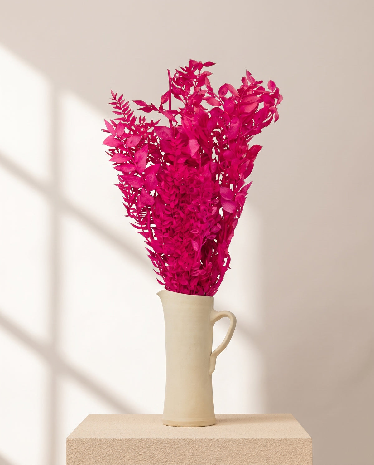 Ruscus preservado fucsia en una jarra de cerámica crema, ambientado. Jarra no incluida.